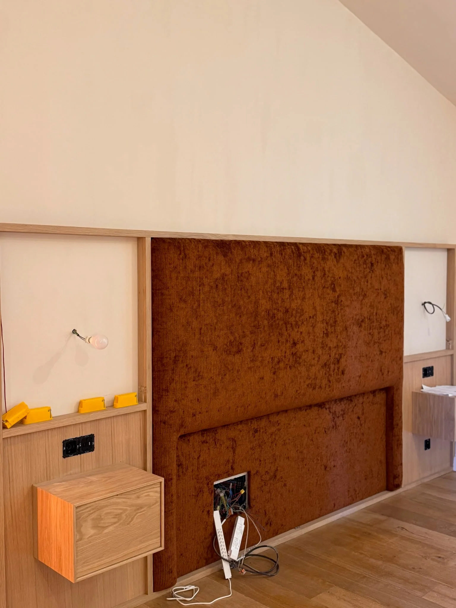 Tête de lit tapissée et chevets en bois en cours d’installation