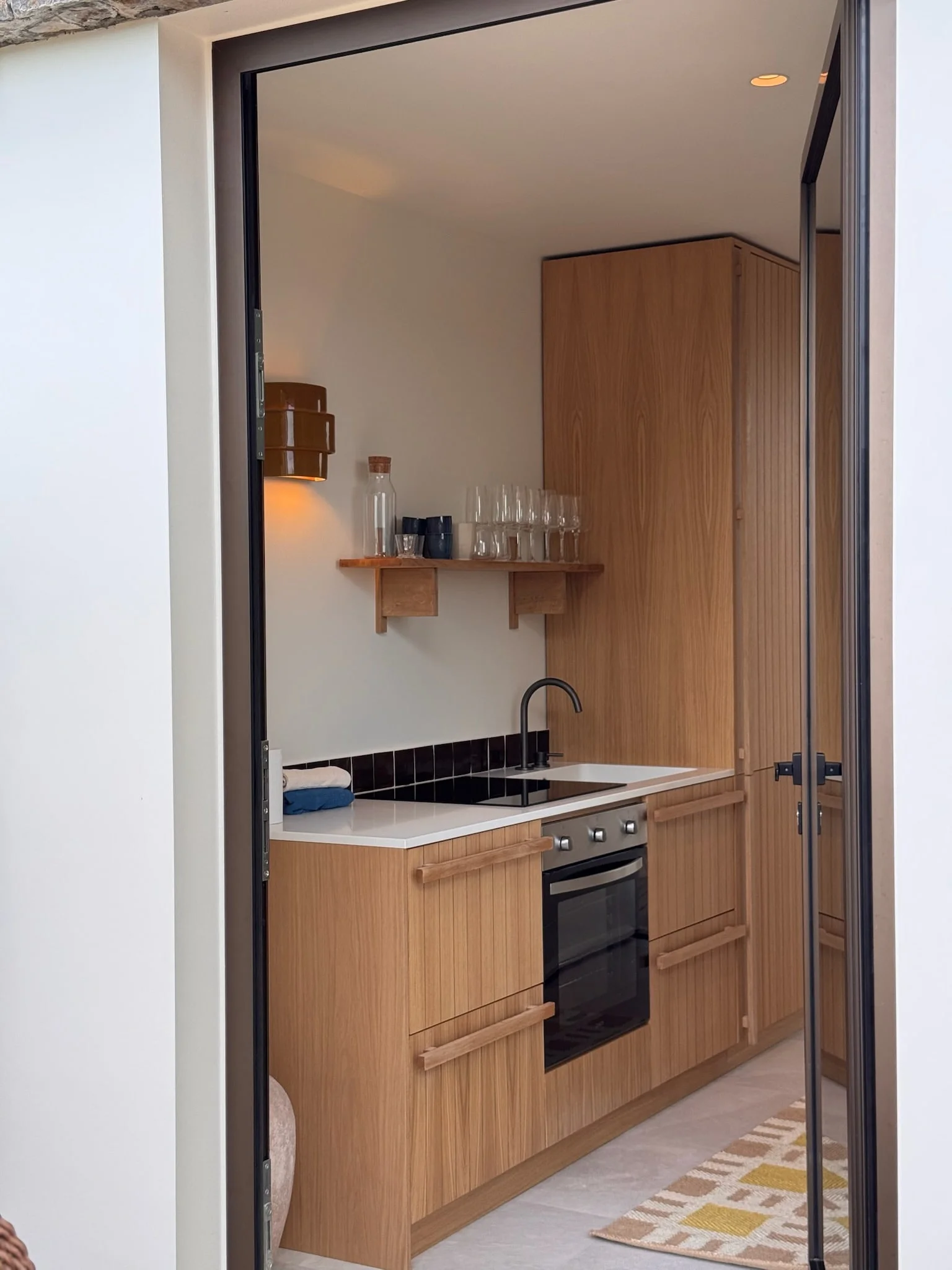 Kitchenette en bois clair derrière une porte vitrée — Anse des Cayes