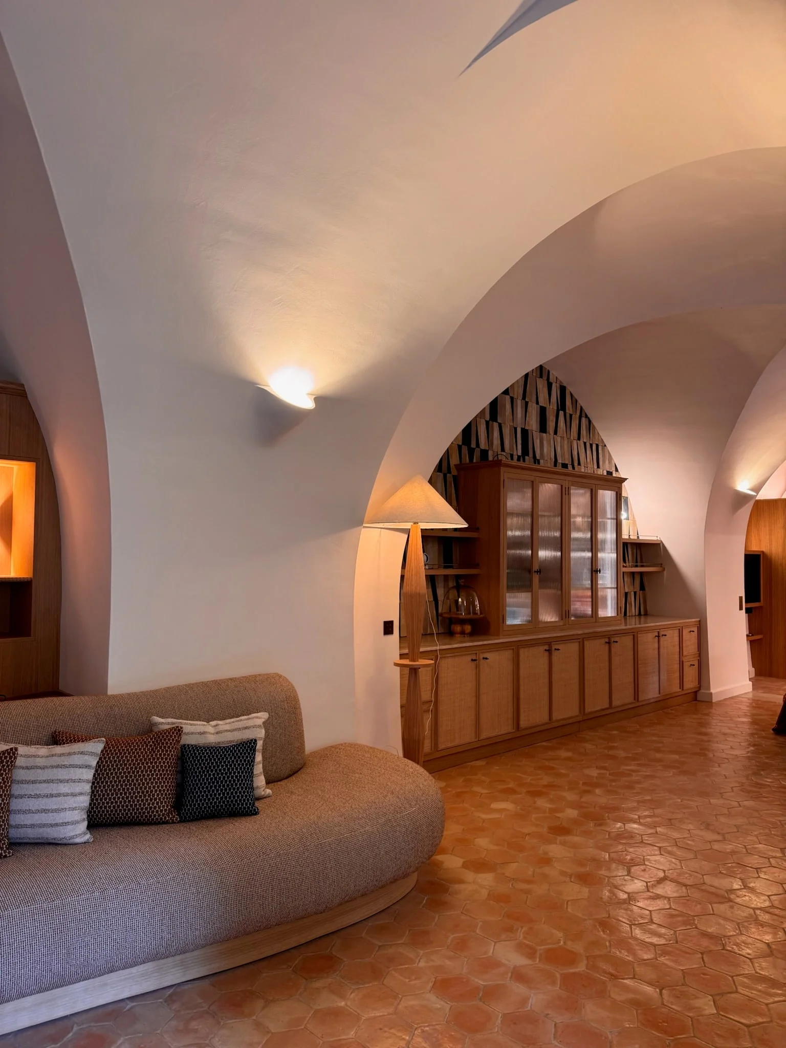 Vaulted living room with curved sofa, terracotta floor and bespoke shelving — Fontaine