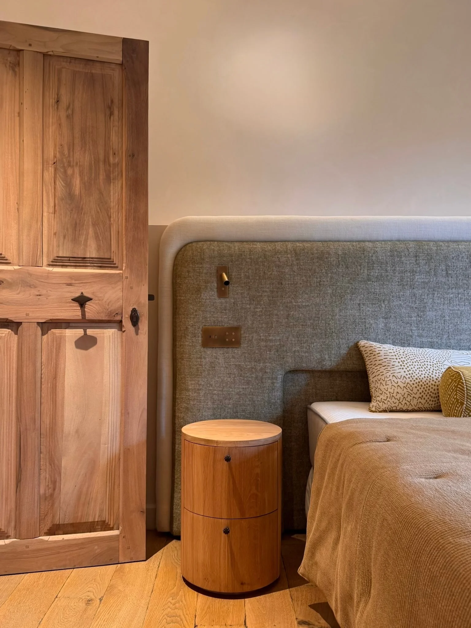 Bedroom with upholstered headboard, round oak bedside table and antique door — Fontaine