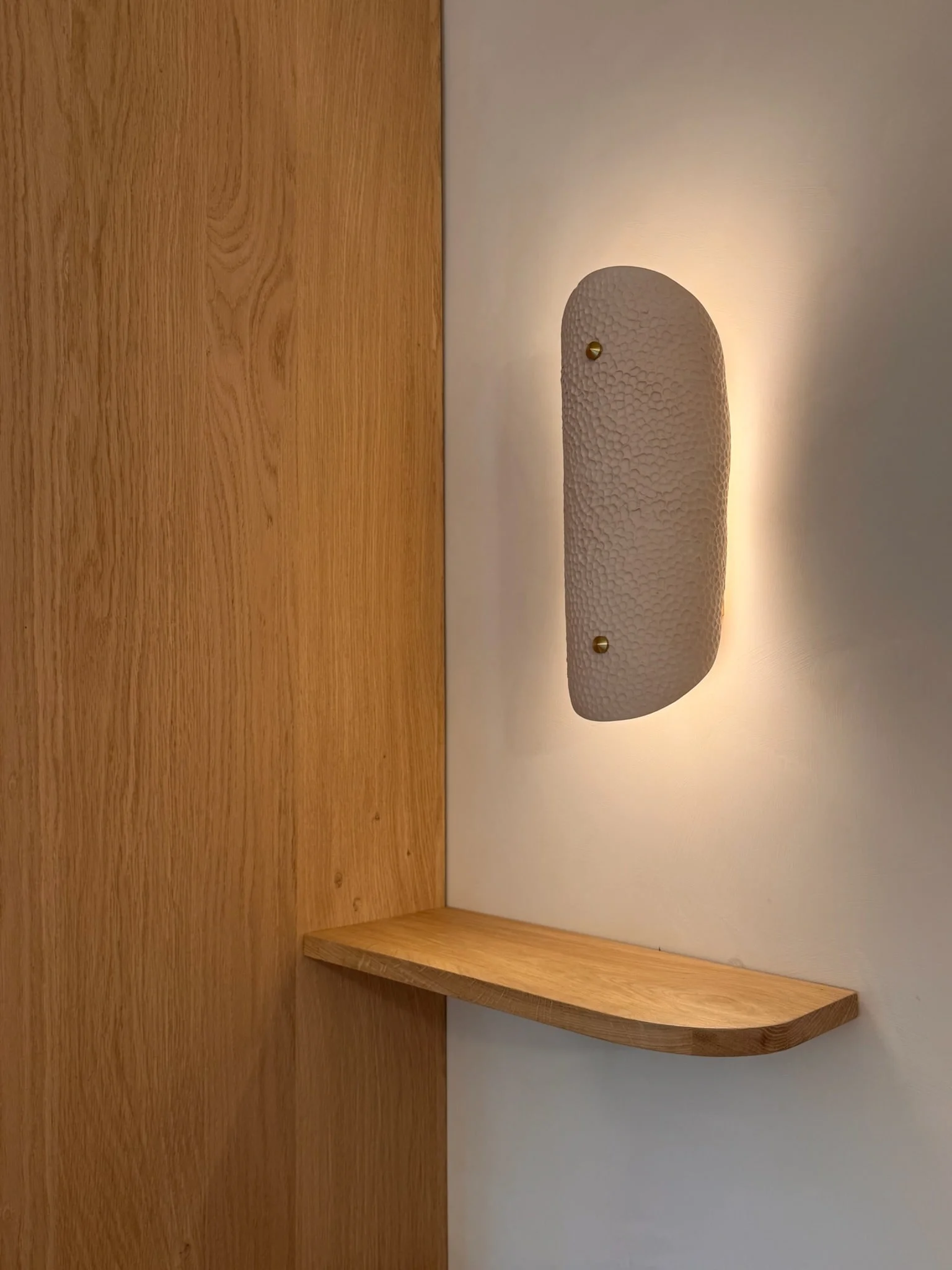 Sculptural wall light above a floating oak shelf — Fontaine