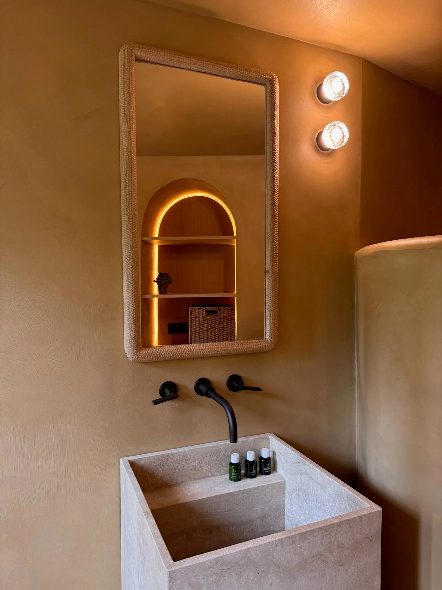 Stone washbasin with arched mirror and black taps — Fontaine