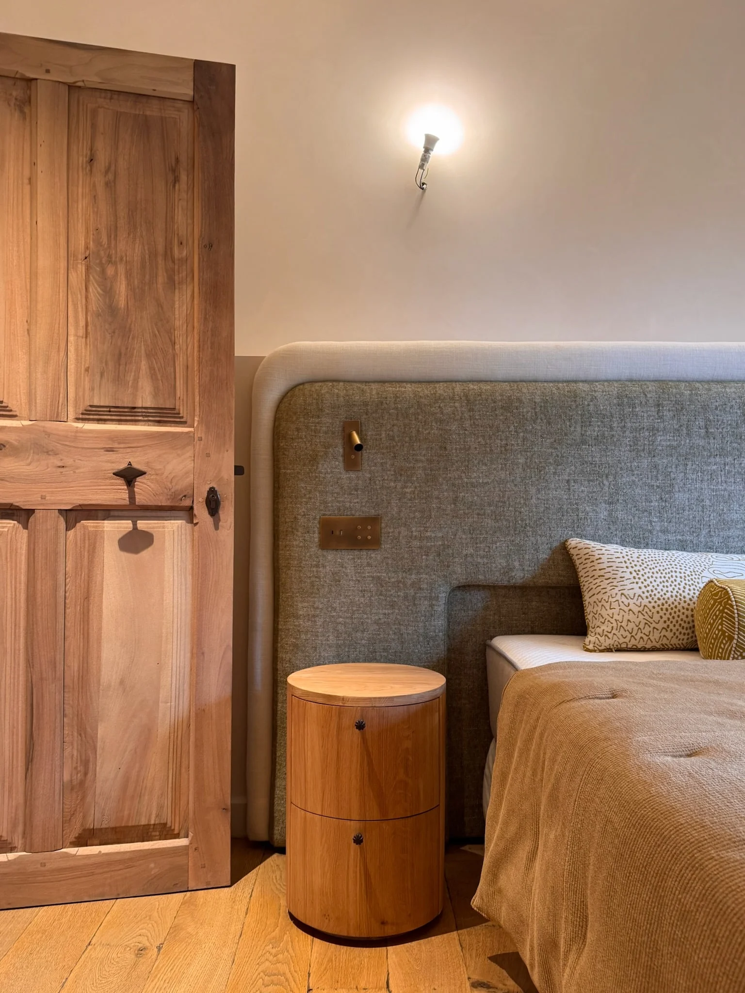 Bedroom with bespoke upholstered headboard and round oak bedside table — Fontaine